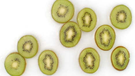 A-lot-of-kiwi-lie-on-white-in-the-background-in-slow-motion-falling-water-splashes.